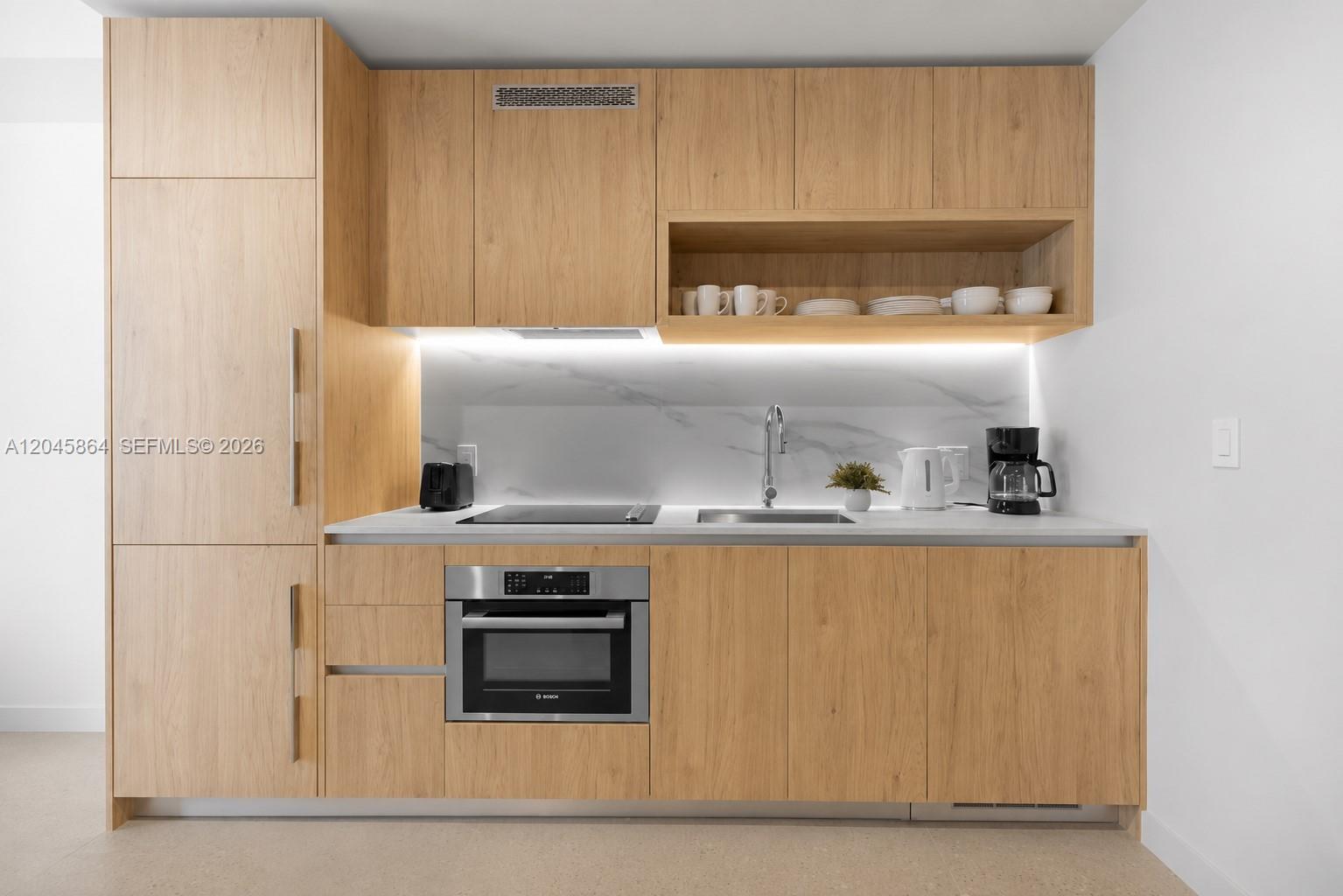 A modern kitchen features light wood cabinetry, a marble backsplash, and stainless steel appliances — 11 NE 6th St # 1712, Miami FL 33132, MIAMI, FL