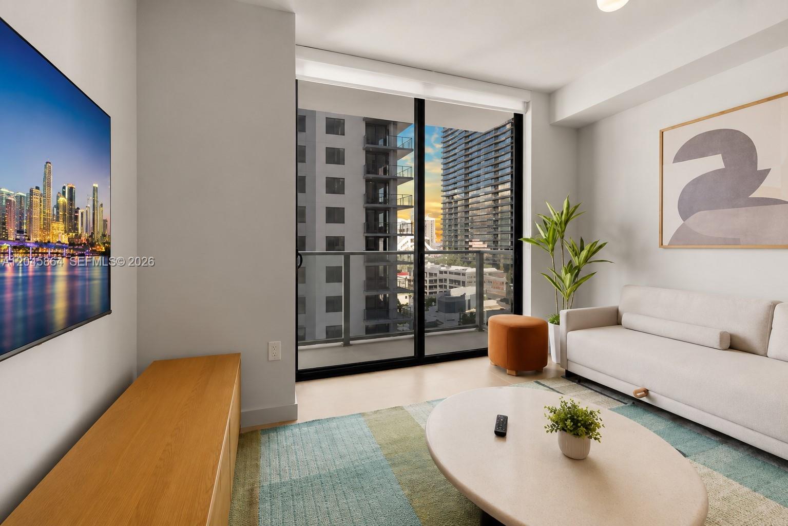 A modern living room features a sofa, coffee table, television, and a balcony with city views — 11 NE 6th St # 1712, Miami FL 33132, MIAMI, FL