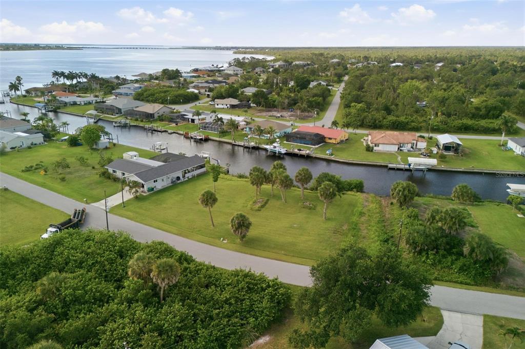 An aerial view shows a waterfront residential neighborhood with a canal, houses, and green lawns — 12397 & 12405 MITCHELL TERRACE, PORT CHARLOTTE, FL