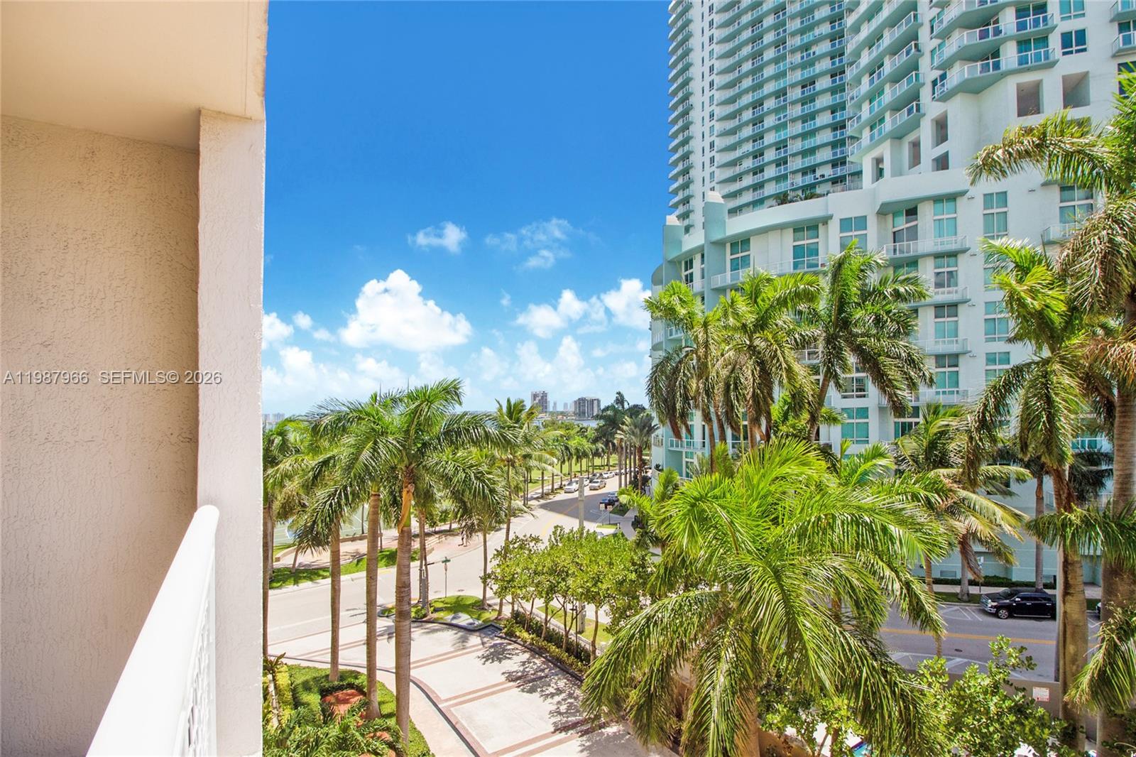A view from a balcony overlooking palm trees, a street, and a tall residential building — 2000 N Bayshore Dr # 506, Miami FL 33137, MIAMI, FL