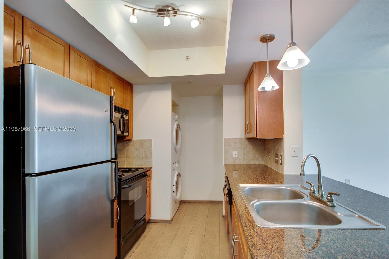 A kitchen features stainless steel appliances, wood cabinets, granite countertops, and a stacked laundry unit — 2000 N Bayshore Dr # 506, Miami FL 33137, MIAMI, FL