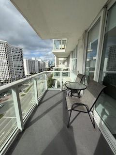 A balcony with a glass railing, two chairs, and a small table overlooking city buildings — 5601 Collins ave # 1219, Miami Beach FL 33140, MIAMI BEACH, FL