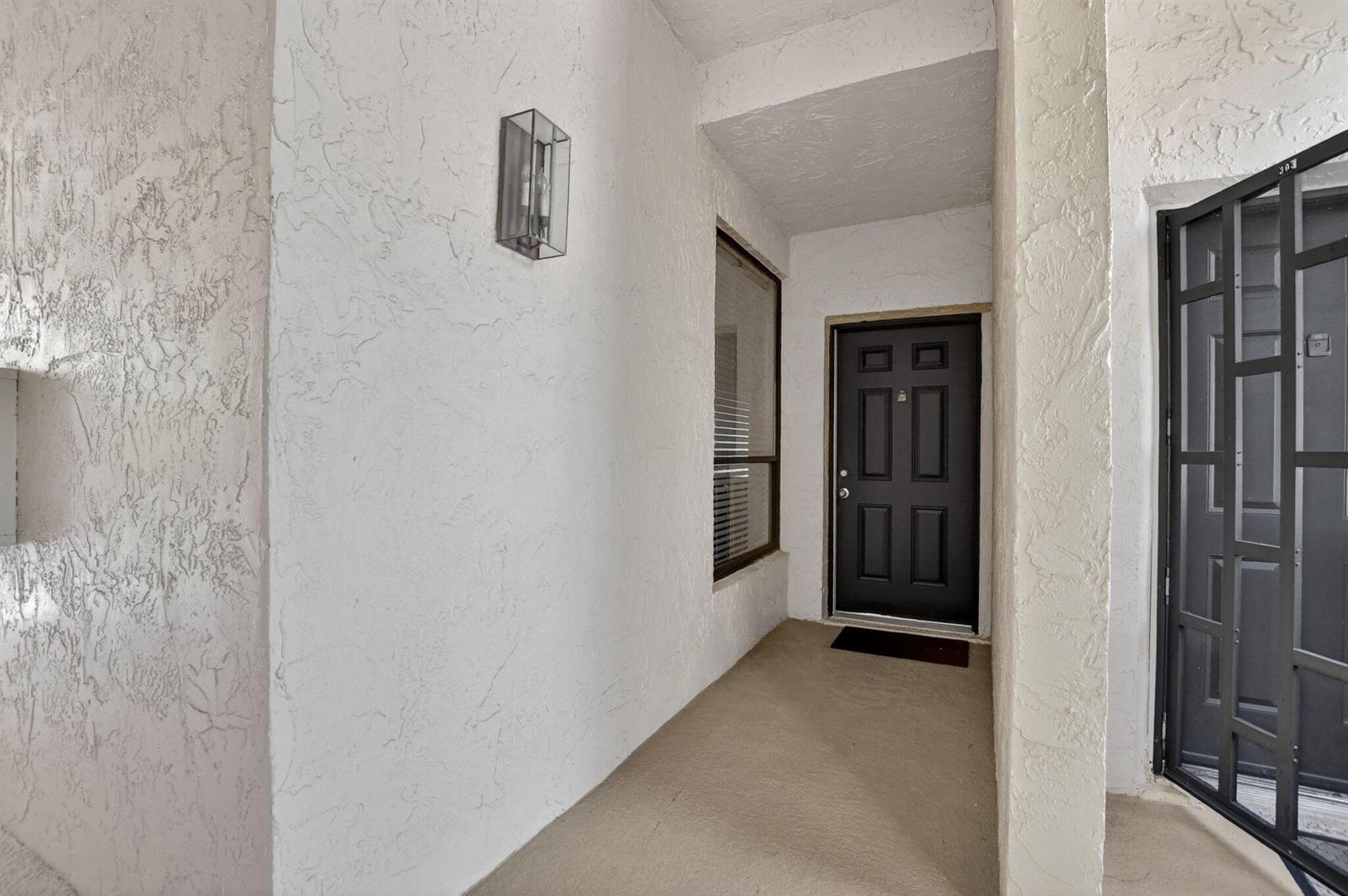 A covered entryway features a black front door, a screen door, and a wall-mounted light — 7472 La Paz Boulevard # 304, Boca Raton FL 33433, BOCA RATON, FL