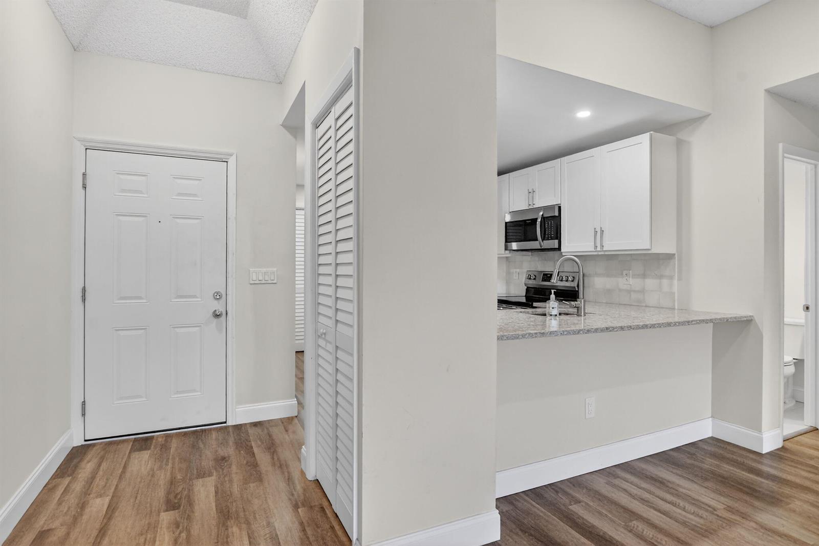 An entryway with wood-look flooring leads to a kitchen featuring white cabinets and granite countertops — 7472 La Paz Boulevard # 304, Boca Raton FL 33433, BOCA RATON, FL