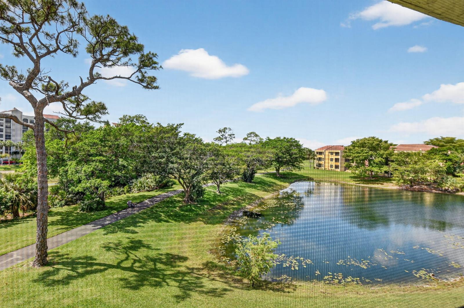 A view from a balcony overlooking a grassy lawn, a pond, and apartment buildings — 7472 La Paz Boulevard # 304, Boca Raton FL 33433, BOCA RATON, FL