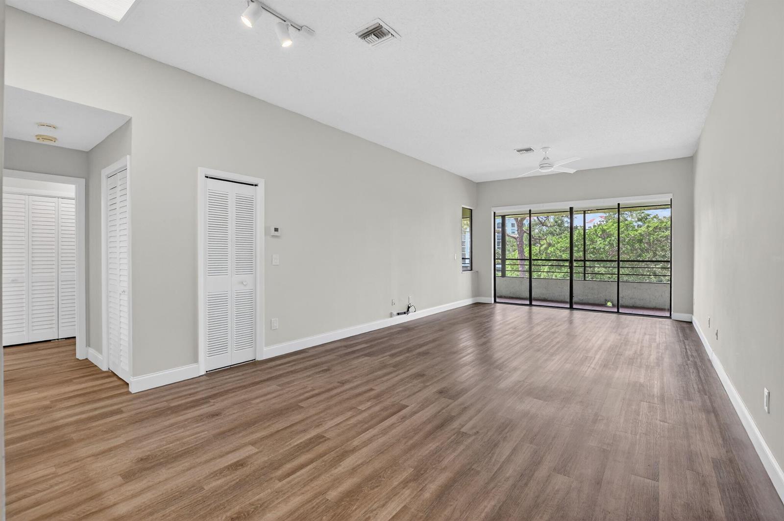 An empty living room with light gray walls, wood-look flooring, and a screened-in balcony — 7472 La Paz Boulevard # 304, Boca Raton FL 33433, BOCA RATON, FL
