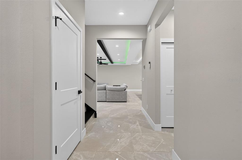A hallway with light tile flooring leads toward a living area with green ceiling lighting — 1309 S CENTER STREET, EUSTIS, FL