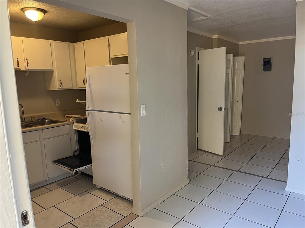 A kitchen with white cabinets and appliances opens into a tiled room with white doors — 231 S ORANGE STREET, SEBRING, FL