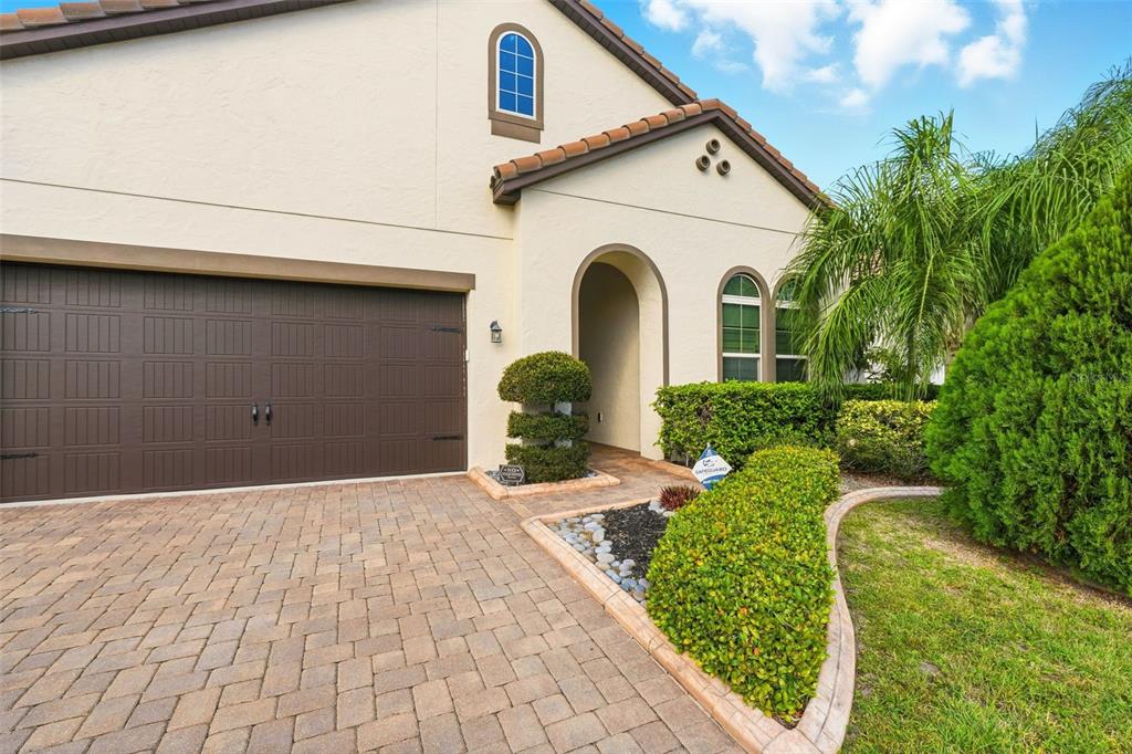 A beige house exterior with a brown garage door, arched entryway, and landscaped front yard — 7945 CHILTON DRIVE, ORLANDO, FL