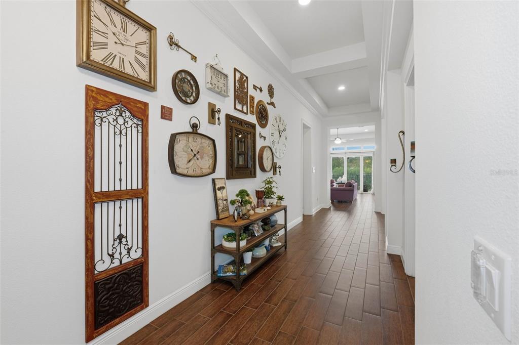 A hallway with wood-look tile flooring features a gallery wall of clocks and decor — 7945 CHILTON DRIVE, ORLANDO, FL