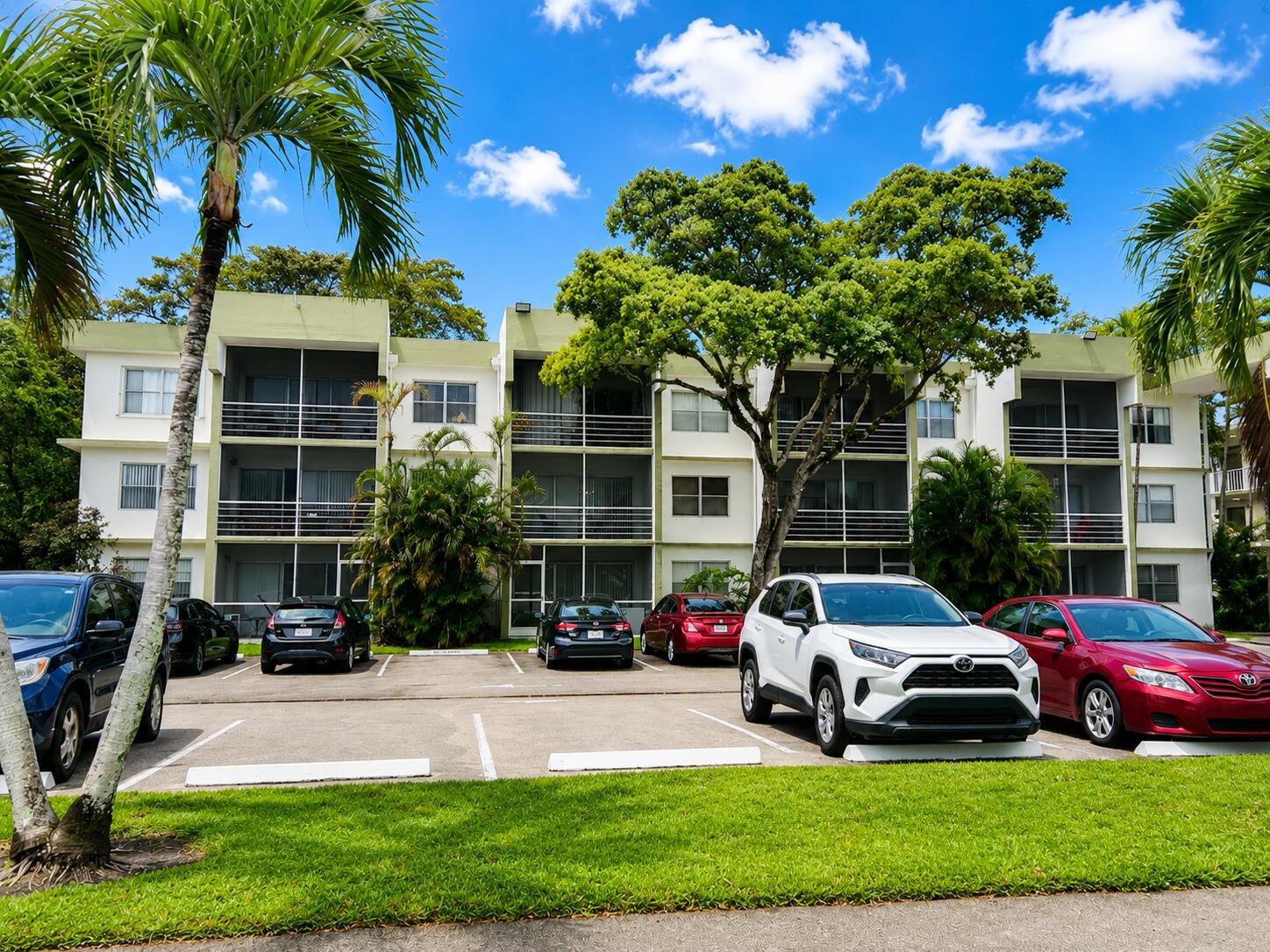 A three-story apartment building with screened balconies sits behind a parking lot with several cars — 4205 N University Drive # 106, Sunrise FL 33351, SUNRISE, FL
