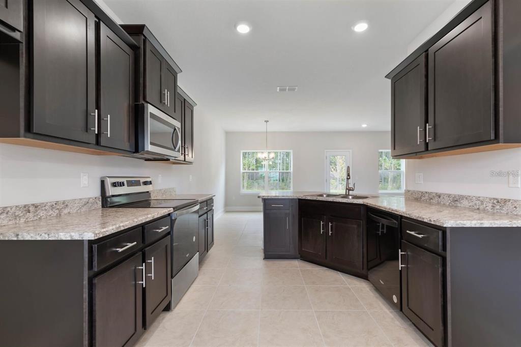 A kitchen features dark wood cabinets, granite countertops, stainless steel appliances, and tile flooring — 59 RADCLIFFE  DRIVE, PALM COAST, FL