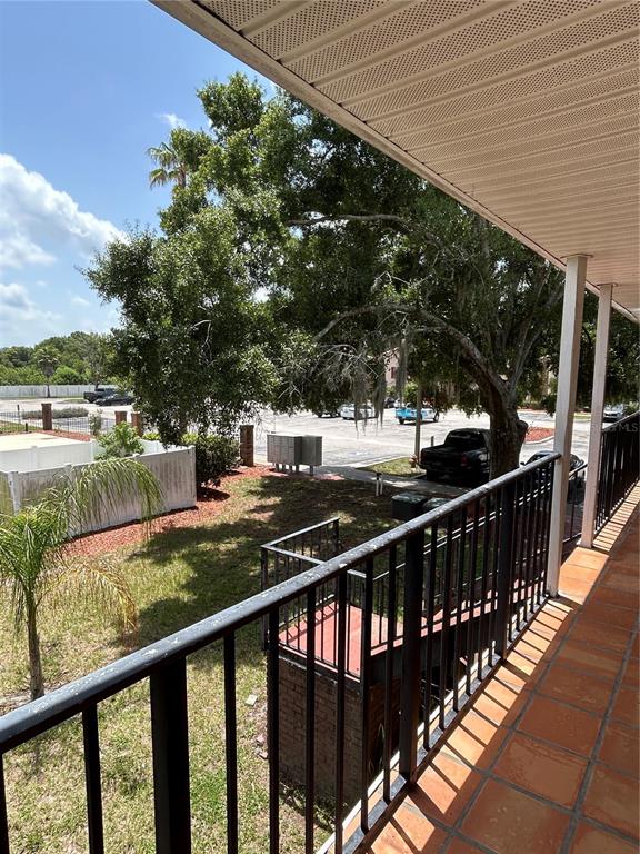A view from a tiled balcony overlooking a grassy area, trees, and a parking lot — 21027 VOYAGER BOULEVARD UNIT 7, LAND O LAKES, FL