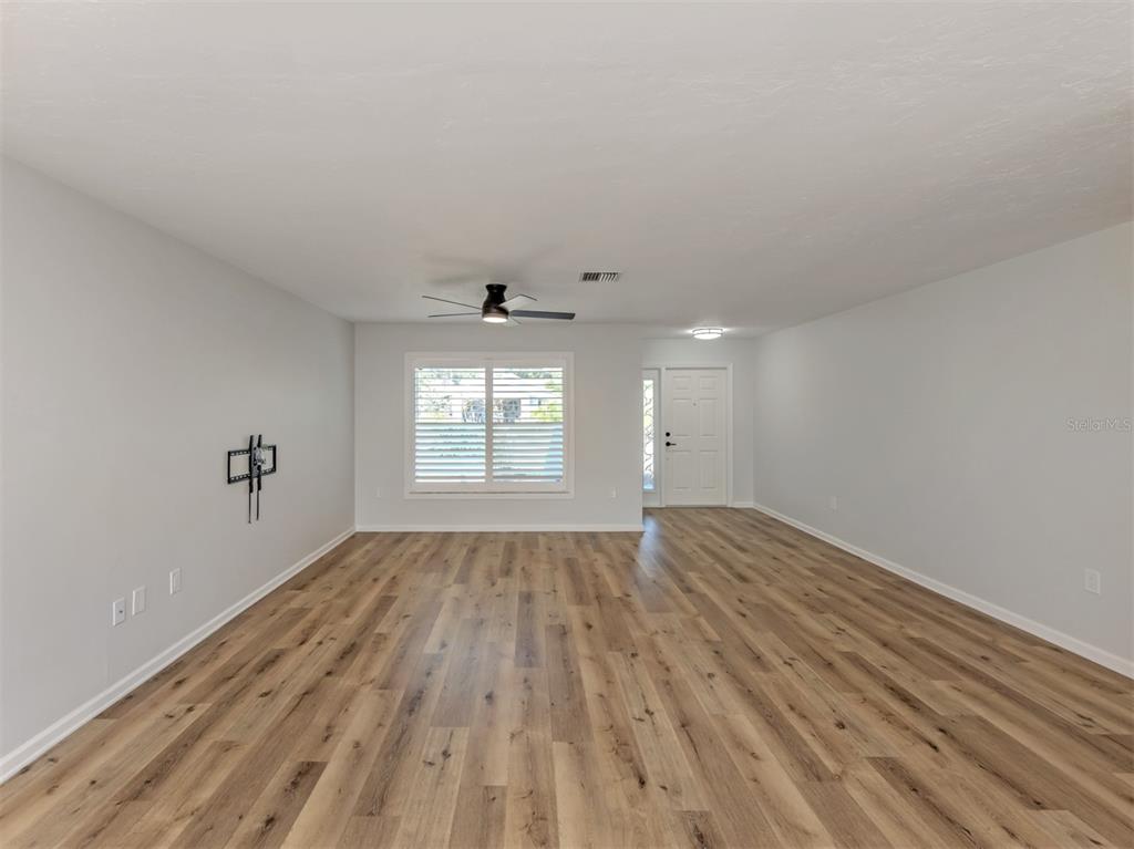An empty living room features light gray walls, wood-look flooring, a ceiling fan, and shutters — 541 CARMEL ROAD, VENICE, FL