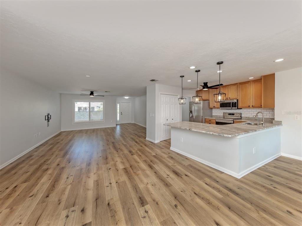 An open-concept kitchen with light wood cabinets and a peninsula overlooks a spacious living area — 541 CARMEL ROAD, VENICE, FL