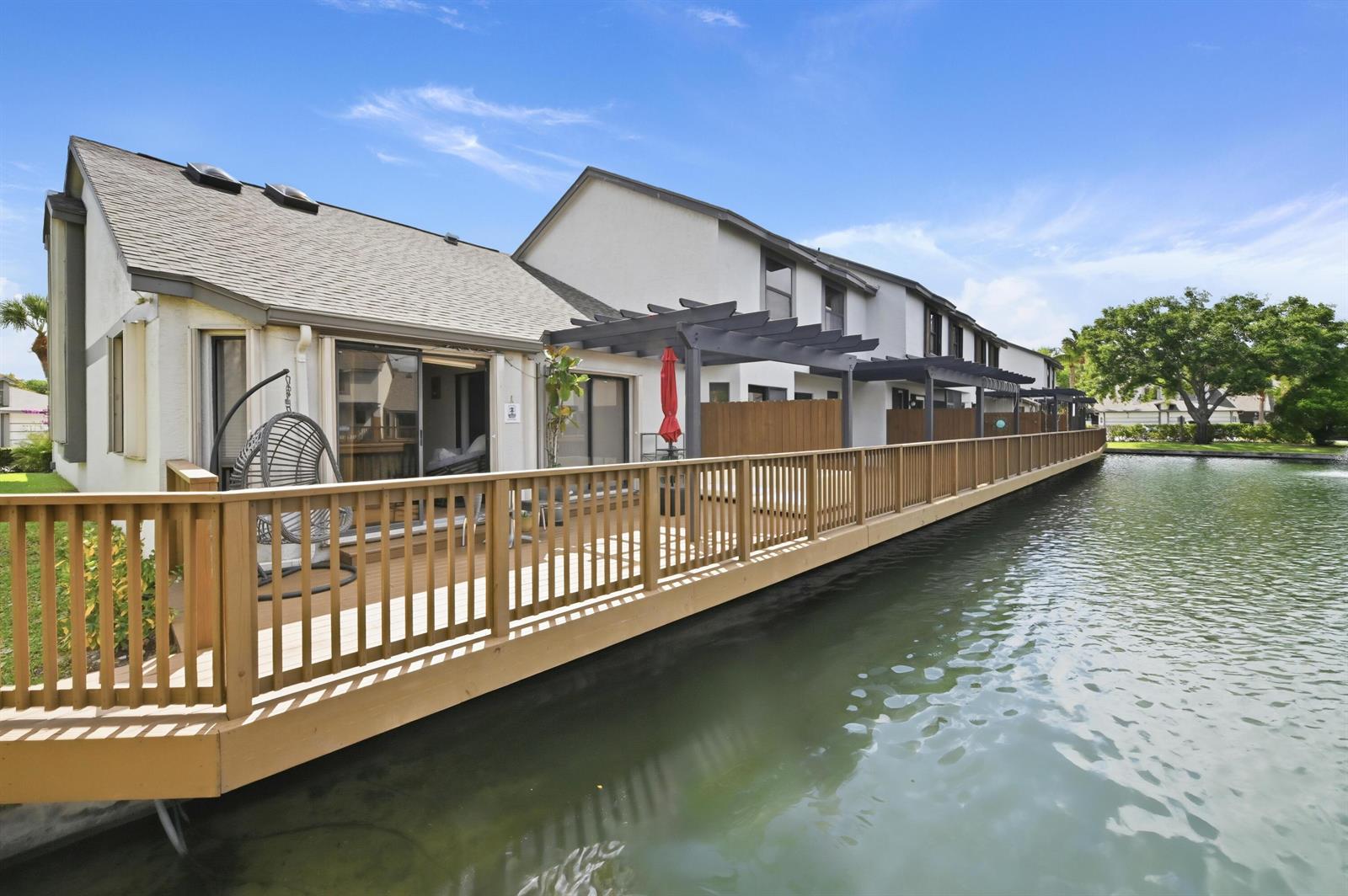 A wooden deck with a railing extends along the back of townhomes overlooking a pond — 1012 Landings Boulevard, FL 33413, FL