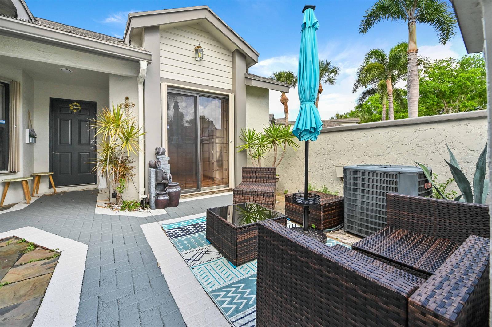 A patio area features gray pavers, wicker furniture, a blue umbrella, and a sliding door — 1012 Landings Boulevard, FL 33413, FL