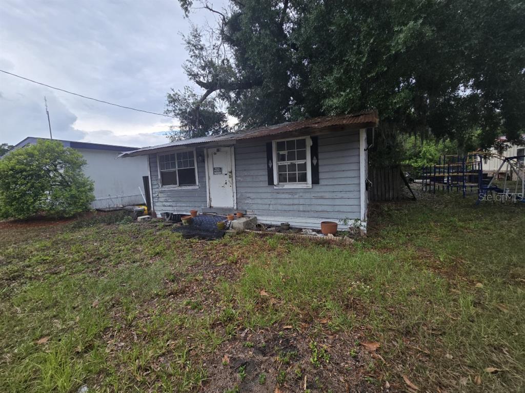 A small, weathered, gray wood-sided house with a metal roof sits on a grassy lot — 515 & 519 RONALD REAGAN PARKWAY, DAVENPORT, FL