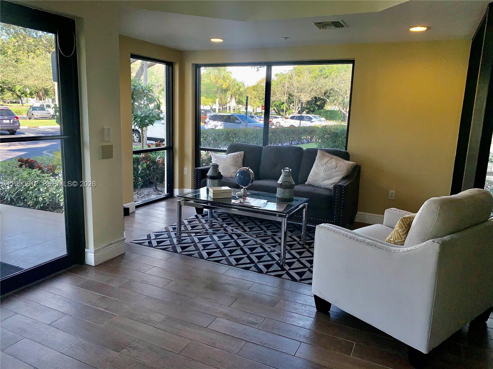 A living room features a dark sofa, a white armchair, and a glass coffee table — 2105 Lavers Cir # 501, Delray Beach FL 33444, DELRAY BEACH, FL