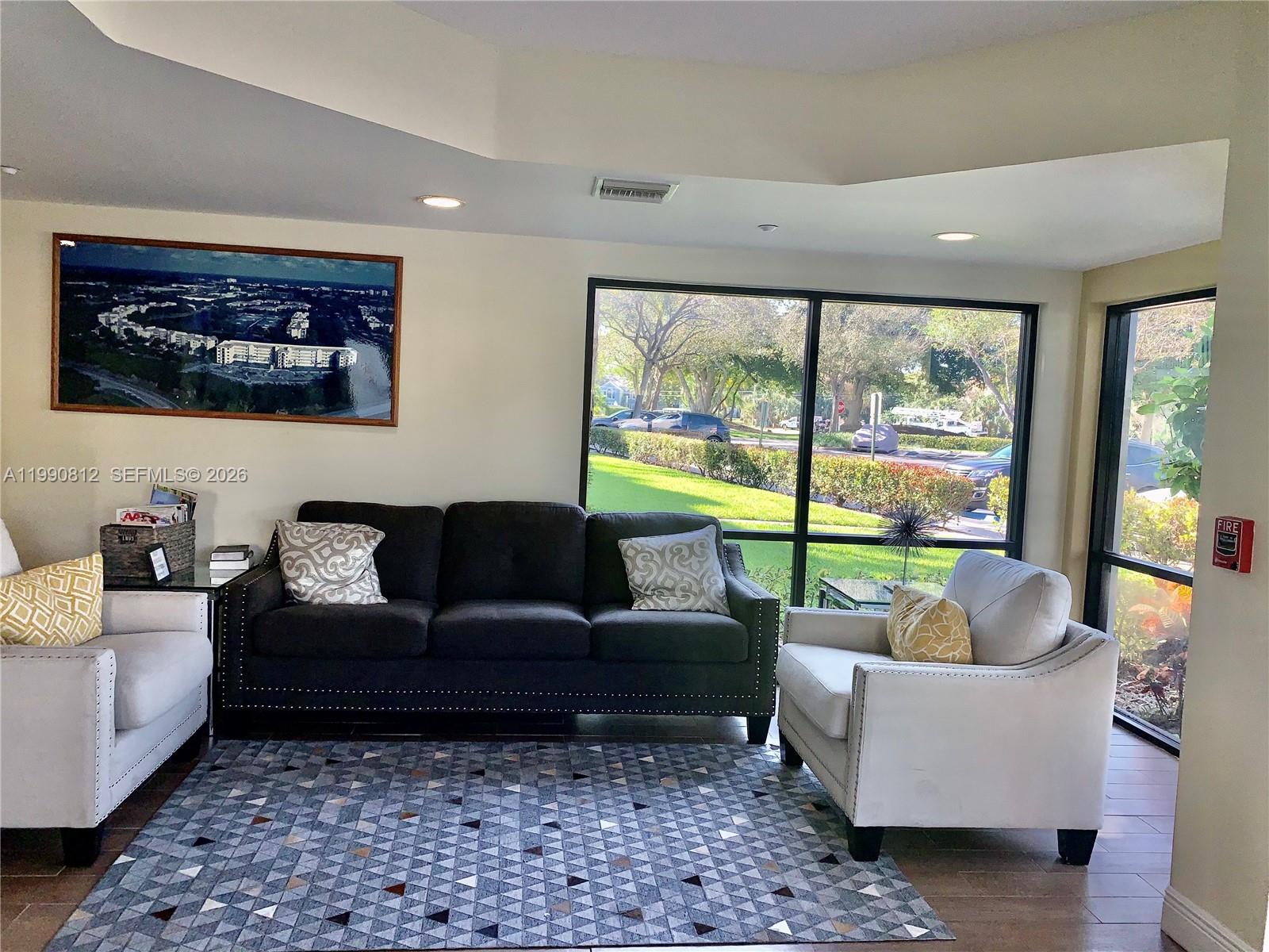 A living room features a dark sofa, two light armchairs, and a geometric area rug — 2105 Lavers Cir # 501, Delray Beach FL 33444, DELRAY BEACH, FL