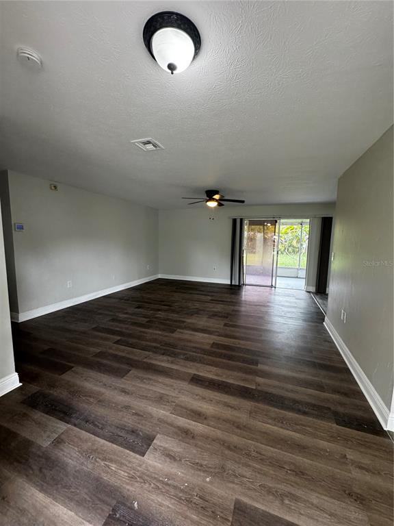 A spacious living room features dark wood-look flooring, a ceiling fan, and sliding glass doors — 6346 SAINT ANDREWS CIRCLE S, FORT MYERS, FL