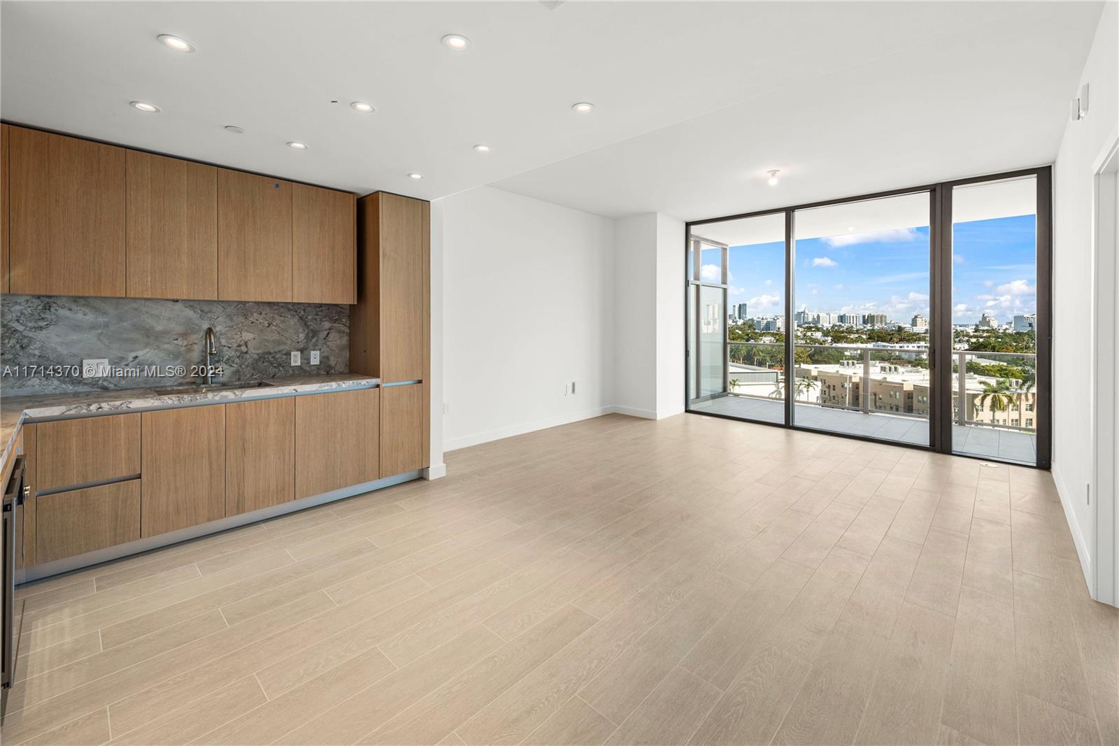 A modern kitchen with wood cabinetry and marble backsplash opens to a balcony with city views — 500 Alton Rd # 908, Miami Beach FL 33139, MIAMI BEACH, FL