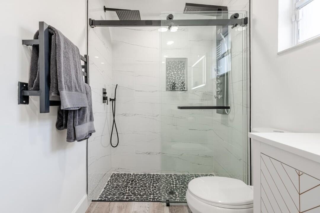 A modern bathroom features a walk-in glass shower with pebble flooring and white marble walls — 1860 Primrose Lane, Wellington FL 33414, WELLINGTON, FL