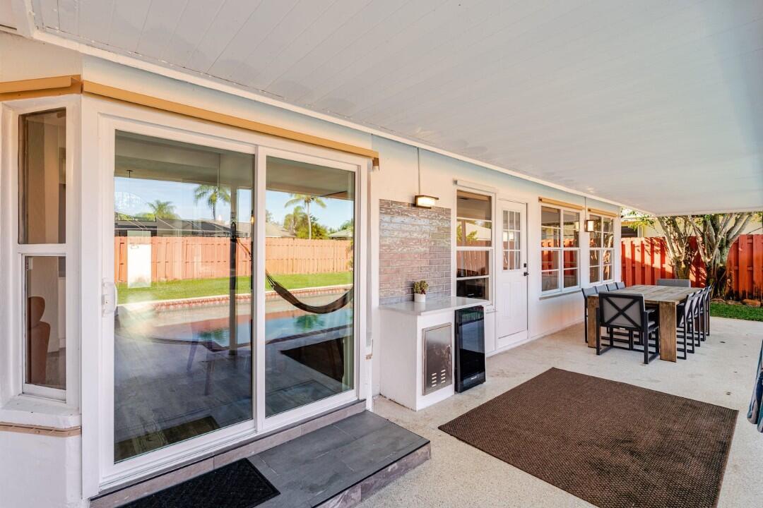 A covered patio features a sliding glass door, an outdoor kitchen area, and dining furniture — 1860 Primrose Lane, Wellington FL 33414, WELLINGTON, FL