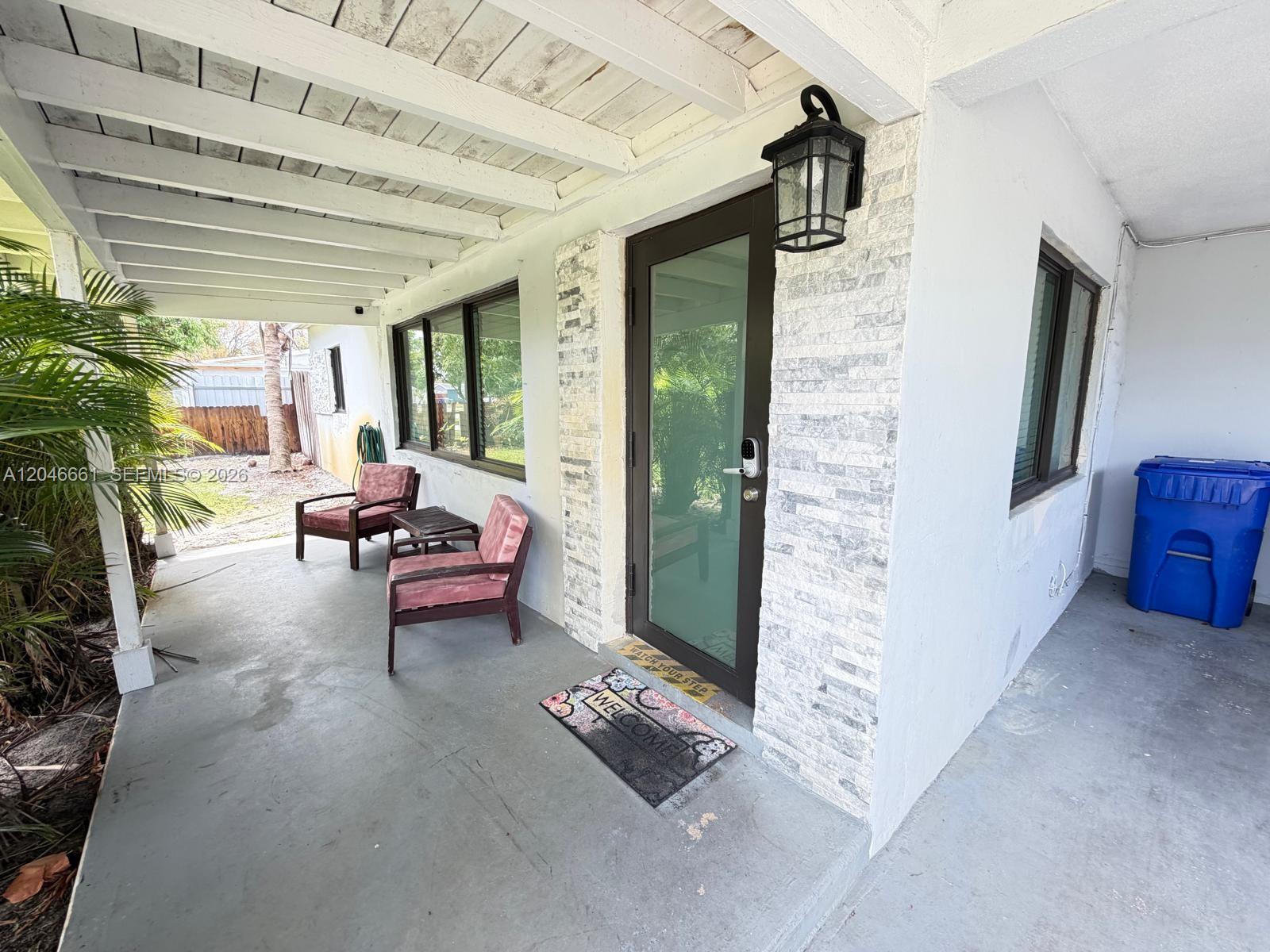 A covered porch features a stone-accented entryway, two chairs, and a blue trash bin — 3351 NE 12th Ter, Pompano Beach FL 33064, POMPANO BEACH, FL