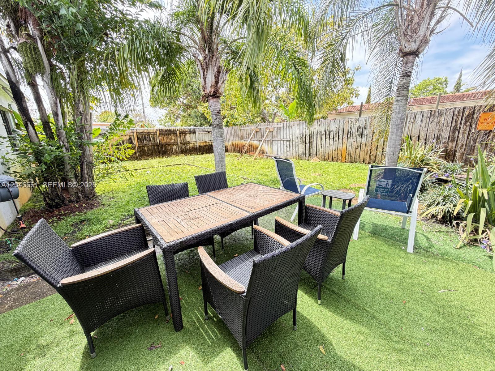 A patio set with a wooden table and wicker chairs sits on artificial grass outdoors — 3351 NE 12th Ter, Pompano Beach FL 33064, POMPANO BEACH, FL
