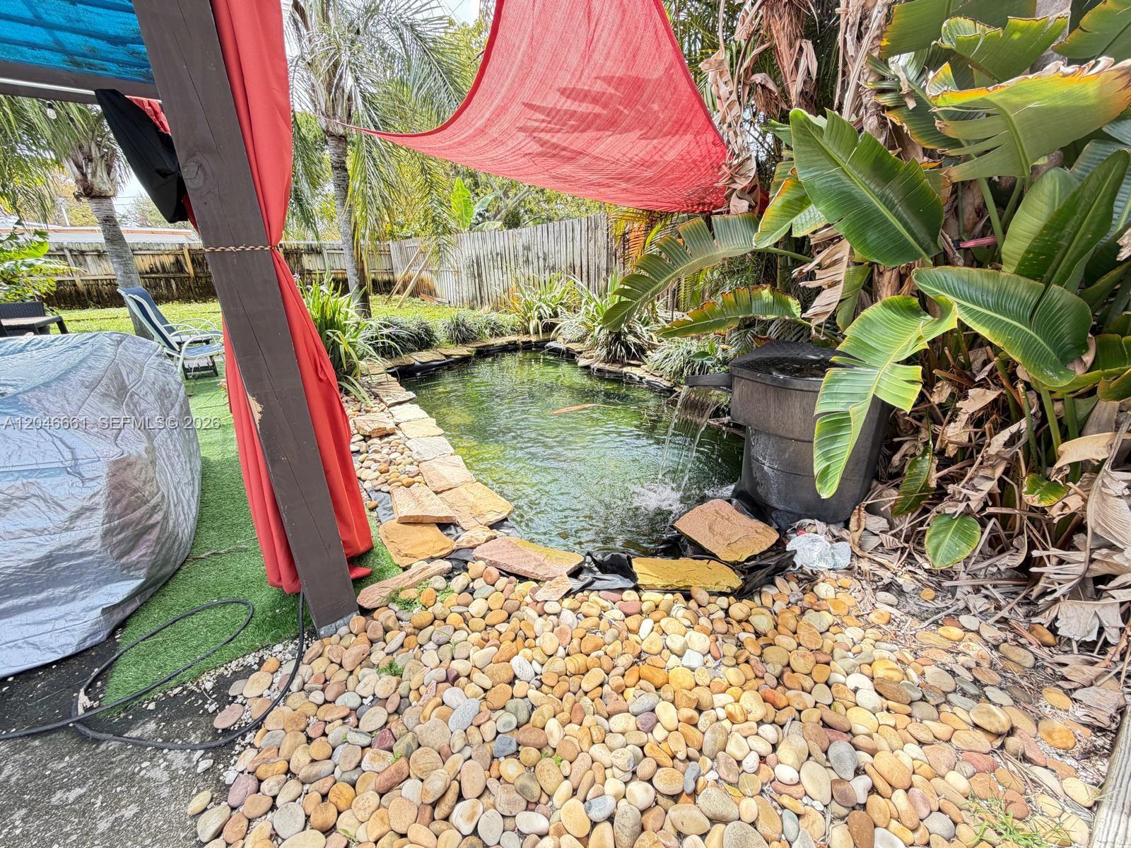 A backyard pond with a waterfall feature is surrounded by stone landscaping and tropical plants — 3351 NE 12th Ter, Pompano Beach FL 33064, POMPANO BEACH, FL