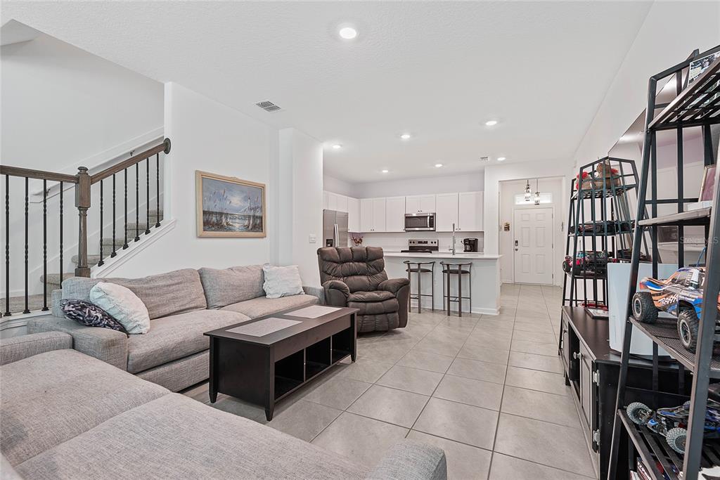 An open-concept living room features a gray sectional sofa, a recliner, and a kitchen beyond — 309 REDBUD ROAD, PALM COAST, FL