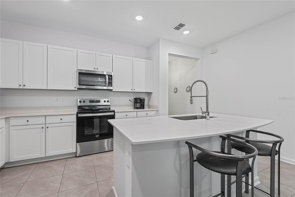 A kitchen features white cabinets, stainless steel appliances, a center island, and tiled flooring — 309 REDBUD ROAD, PALM COAST, FL