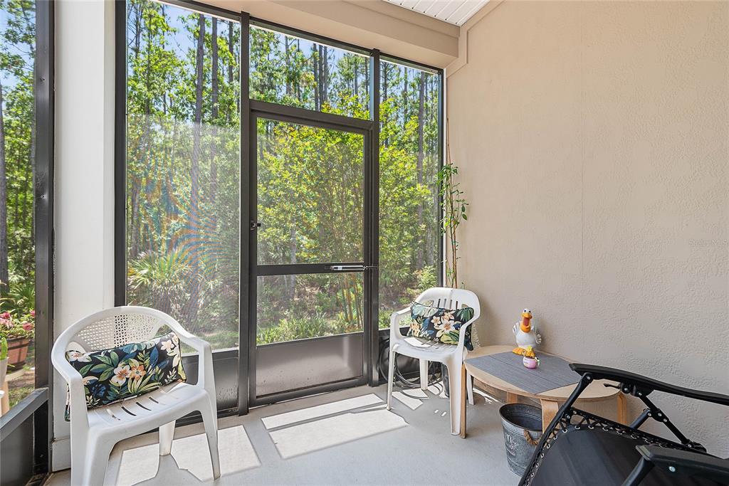 A screened-in porch features white plastic chairs, a small table, and a view of woods — 309 REDBUD ROAD, PALM COAST, FL