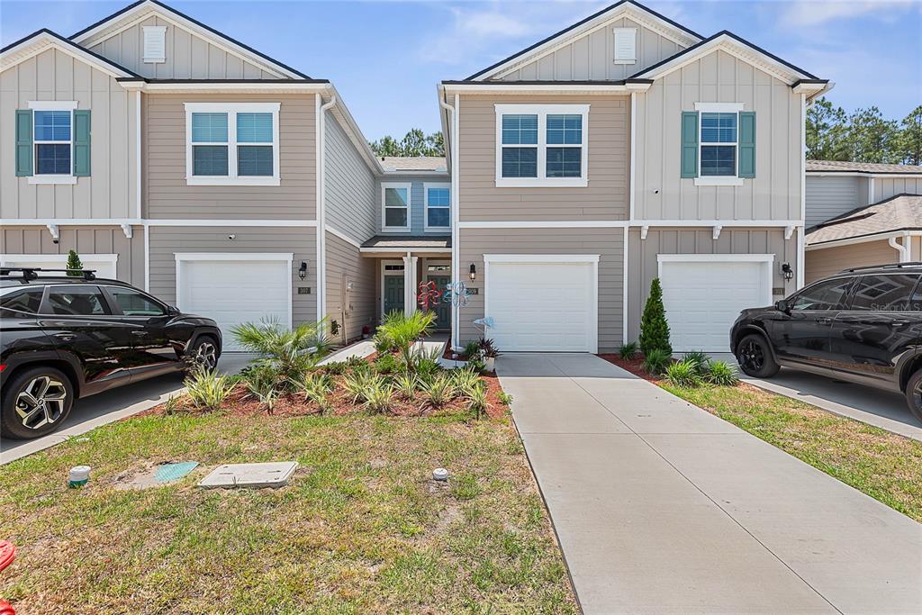 A two-story townhouse exterior features beige siding, white garage doors, and a shared front walkway — 309 REDBUD ROAD, PALM COAST, FL
