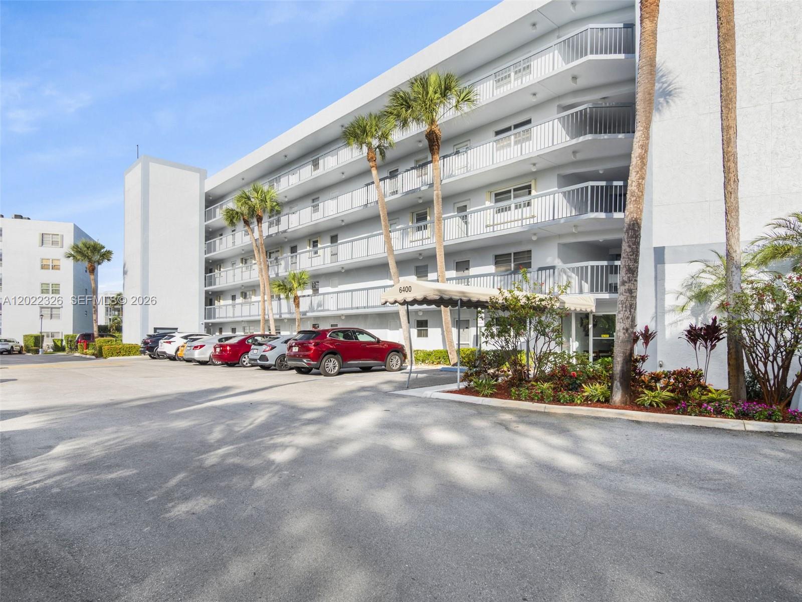 A multi-story apartment building with a parking lot and palm trees in front — 6400 NW 2nd Ave # 117, Boca Raton FL 33487, BOCA RATON, FL