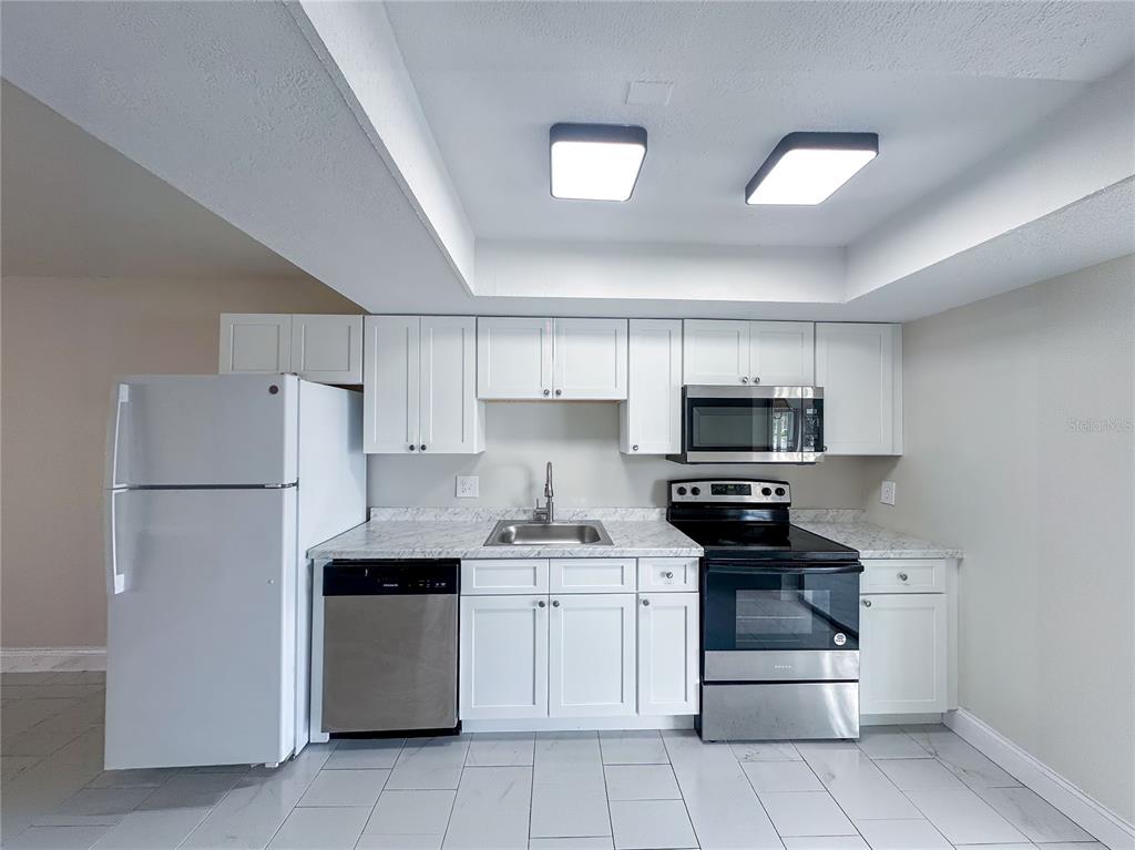 A kitchen features white cabinets, stainless steel appliances, and light-colored countertops — 15 W COUNTRY COVE, KISSIMMEE, FL