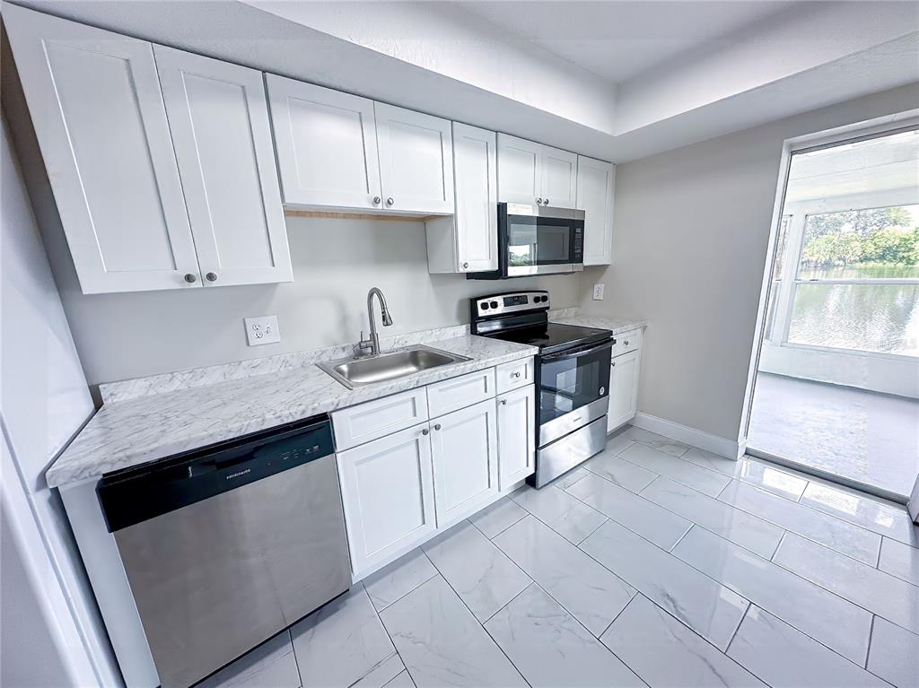 A kitchen features white cabinets, marble-look countertops, stainless steel appliances, and light tile flooring — 15 W COUNTRY COVE, KISSIMMEE, FL
