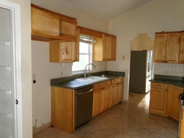 A kitchen features light wood cabinets, a stainless steel dishwasher, and tile flooring — 3298 AMACA CIRCLE, ORLANDO, FL