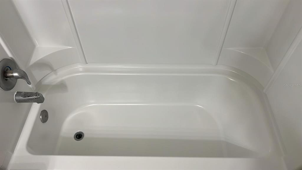 A white bathtub with a shower surround and chrome fixtures is shown in a bathroom — 6004 WESTGATE DRIVE UNIT 104, ORLANDO, FL