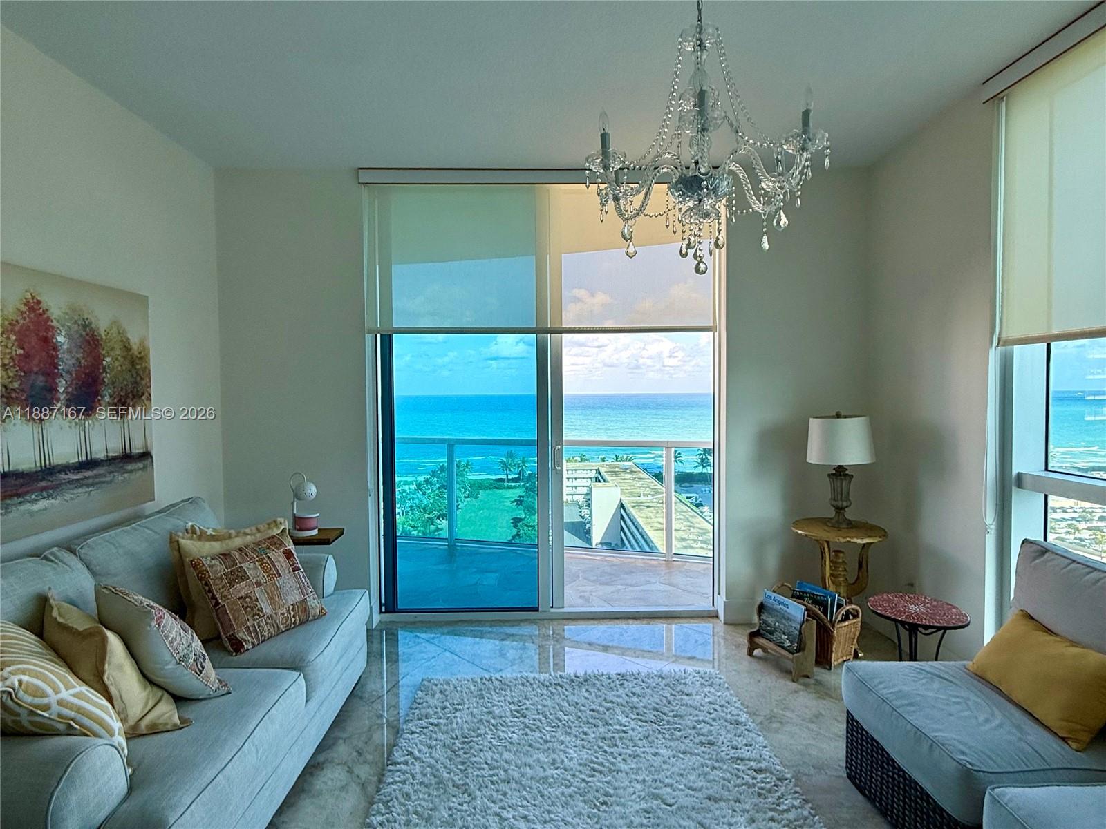 A living room features a chandelier, marble floors, and a balcony overlooking the ocean — 1945 S Ocean Dr # 1201, Hallandale Beach FL 33009, HALLANDALE BEACH, FL