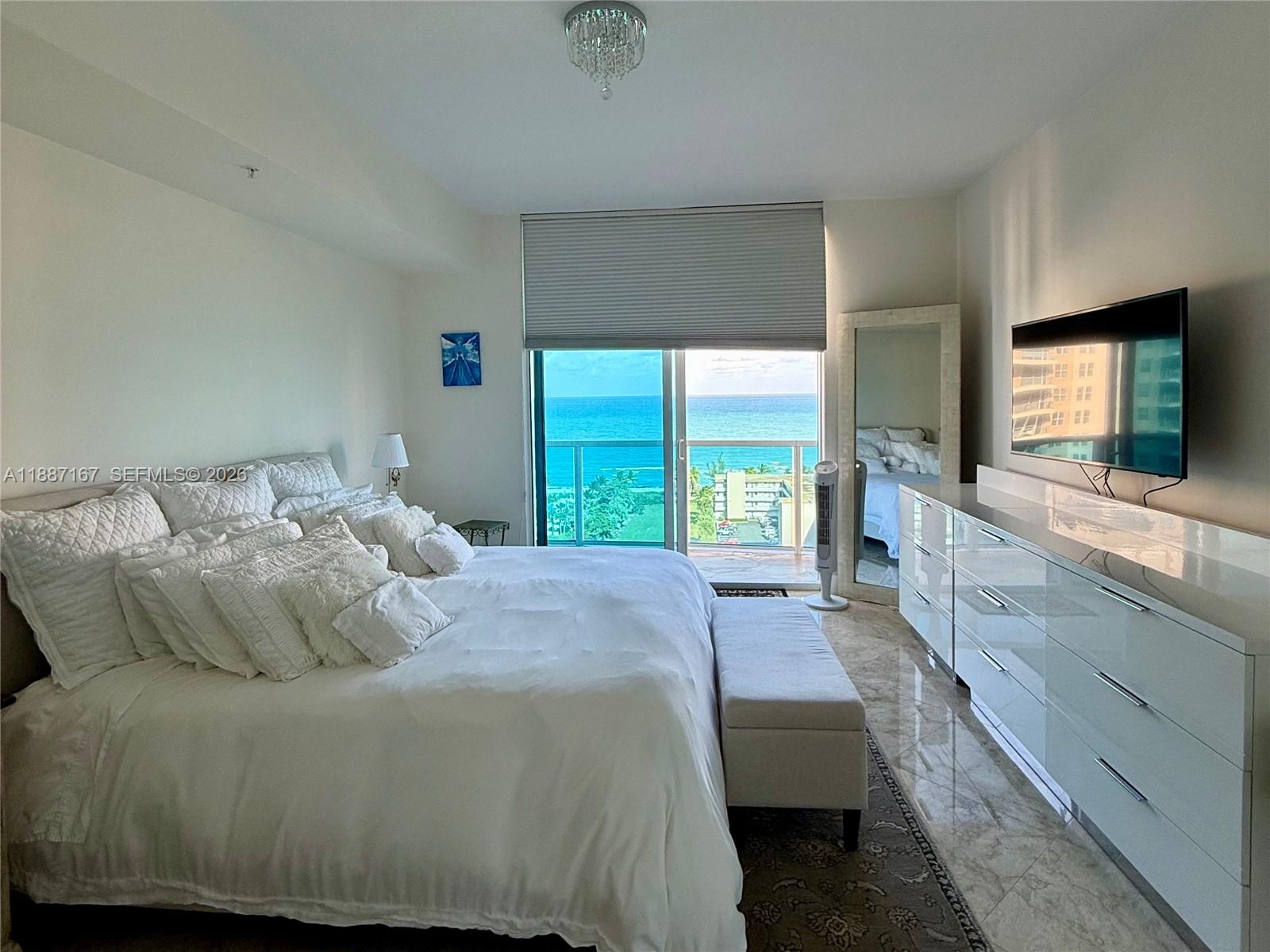 A bedroom features a white bed, a long dresser, and a balcony overlooking the ocean — 1945 S Ocean Dr # 1201, Hallandale Beach FL 33009, HALLANDALE BEACH, FL