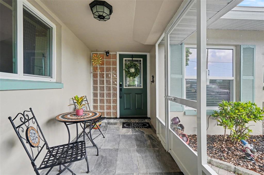 A covered front porch features tile flooring, a green door, and a small bistro set — 5603 LOWN STREET N, ST PETERSBURG, FL