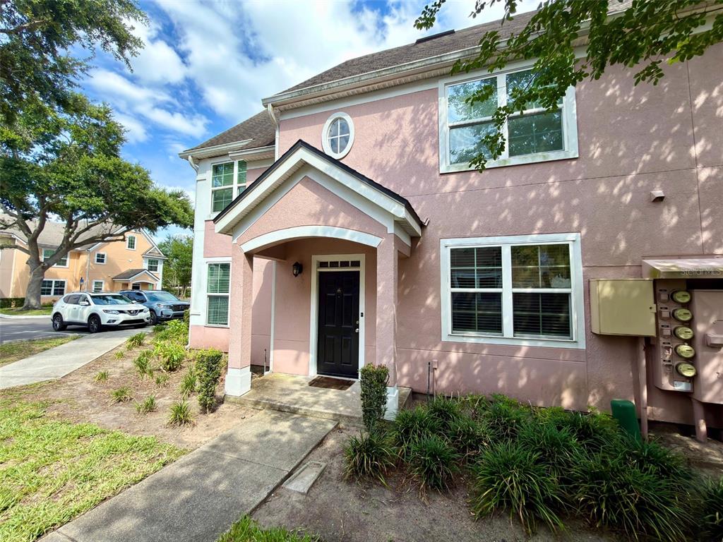 A two-story pink stucco building features a covered entryway, a black front door, and windows — 3420 GREENWICH VILLAGE BOULEVARD UNIT 204, ORLANDO, FL