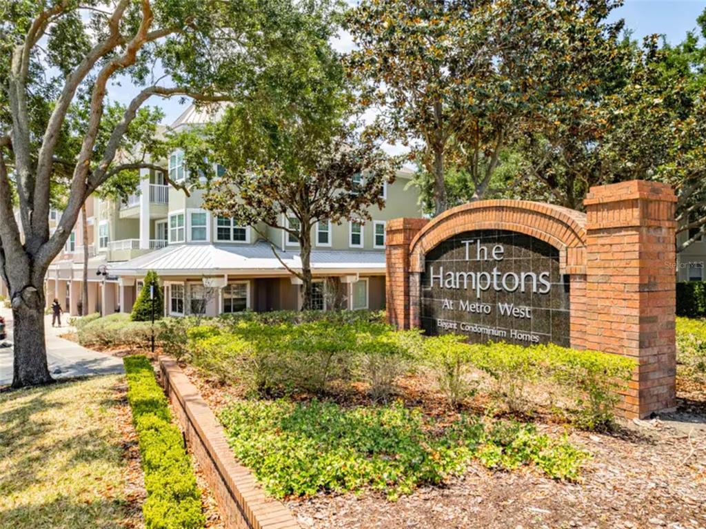 A brick sign for The Hamptons at Metro West stands before a multi-story apartment building — 3420 GREENWICH VILLAGE BOULEVARD UNIT 204, ORLANDO, FL