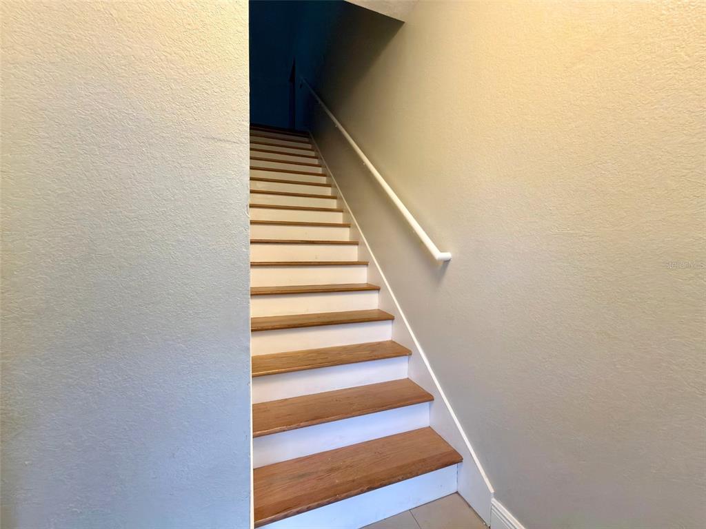 A staircase with wooden treads and white risers leads upward between two beige walls — 3420 GREENWICH VILLAGE BOULEVARD UNIT 204, ORLANDO, FL