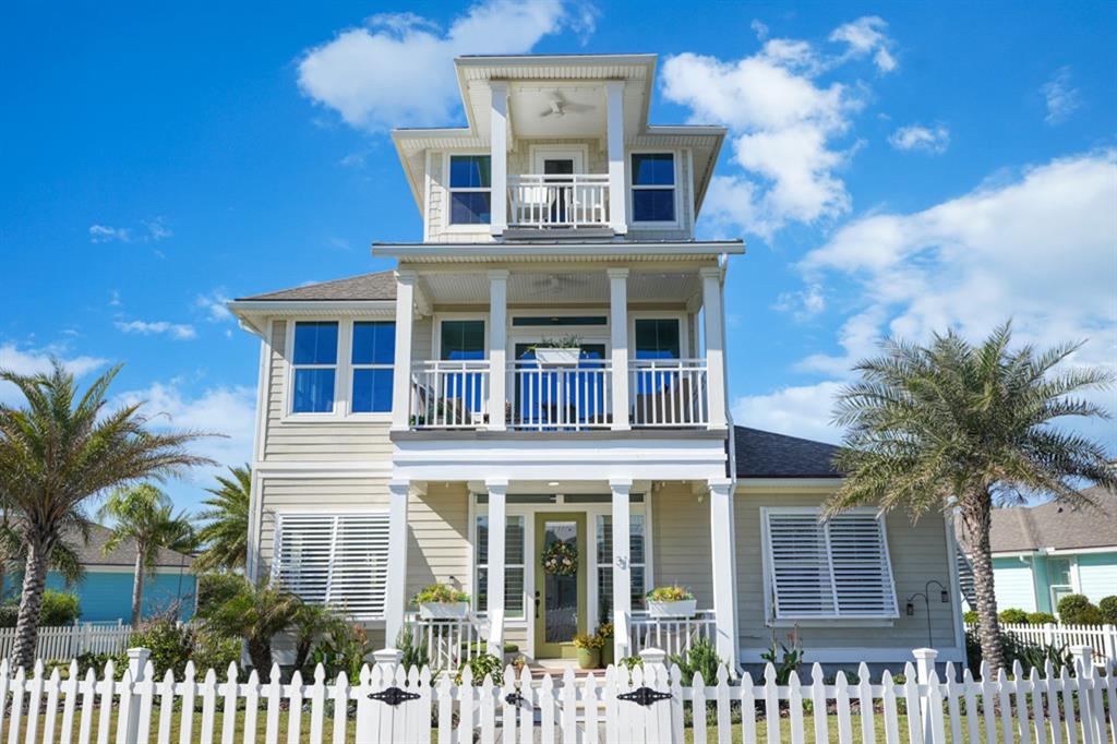 A three-story house with a white picket fence, porches, and palm trees under a blue sky — 31 BEACH HAVEN PARKWAY, PALM COAST, FL