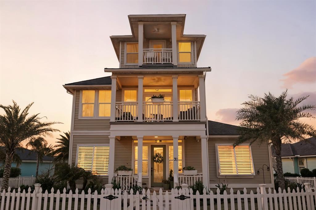 A three-story house with a white picket fence, multiple balconies, and warm interior lighting — 31 BEACH HAVEN PARKWAY, PALM COAST, FL