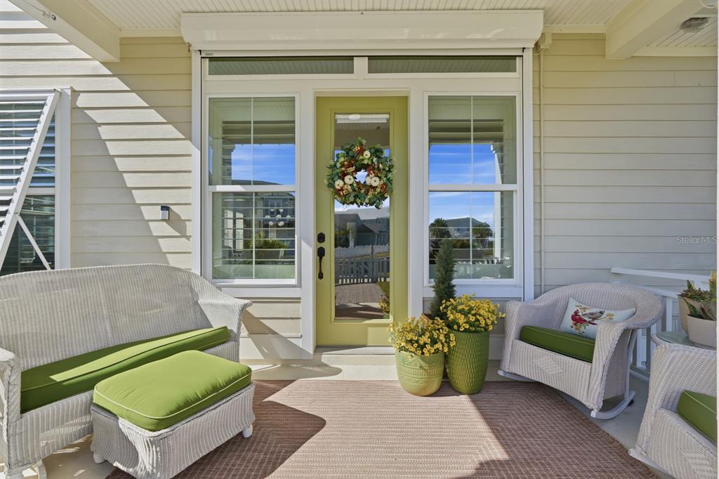 A covered porch features white wicker furniture with green cushions and a glass-paneled door — 31 BEACH HAVEN PARKWAY, PALM COAST, FL