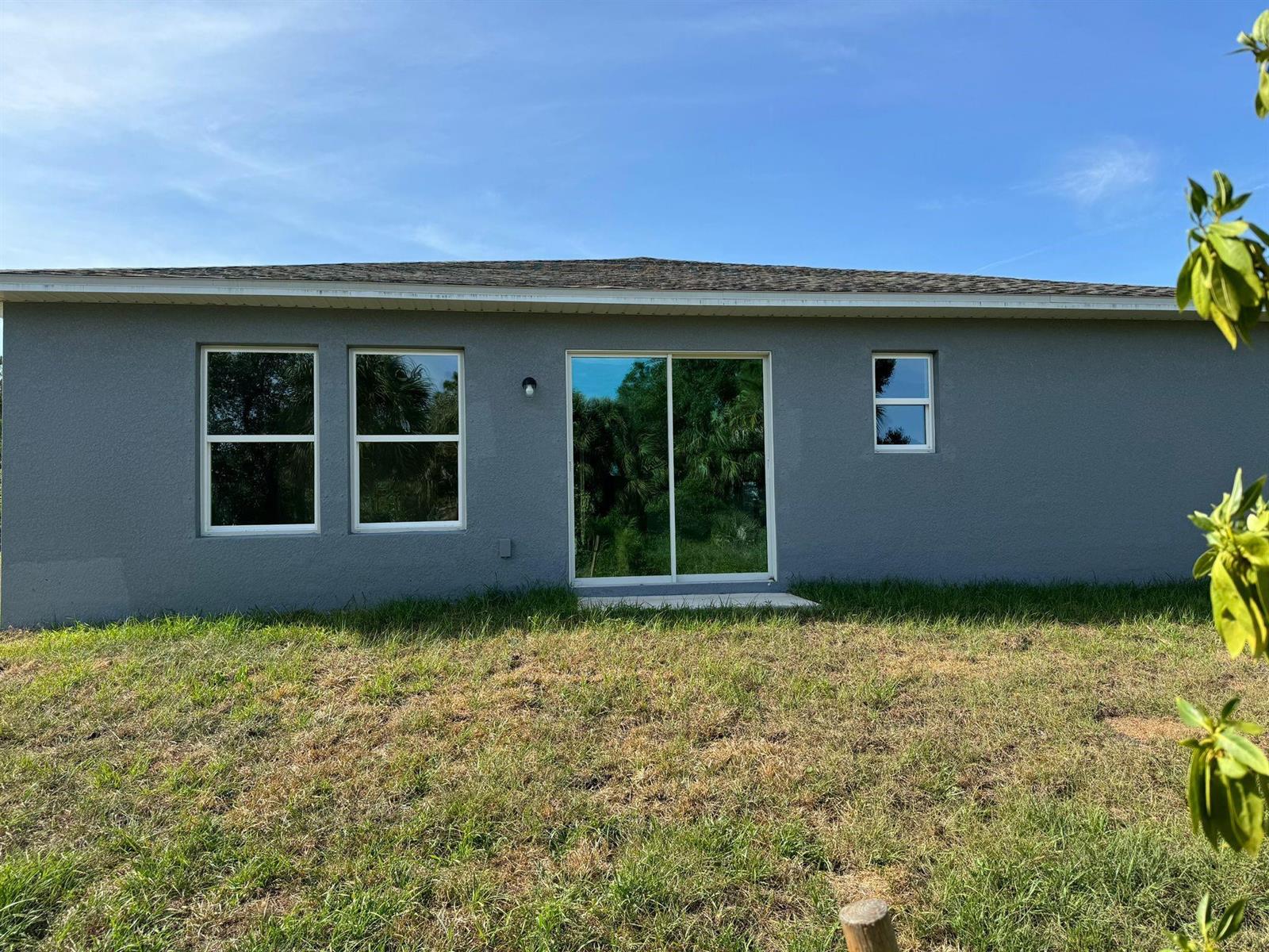 The exterior of a gray stucco house features two windows, a sliding glass door, and grass — 6050 Pecan Circle, FL 33935, FL